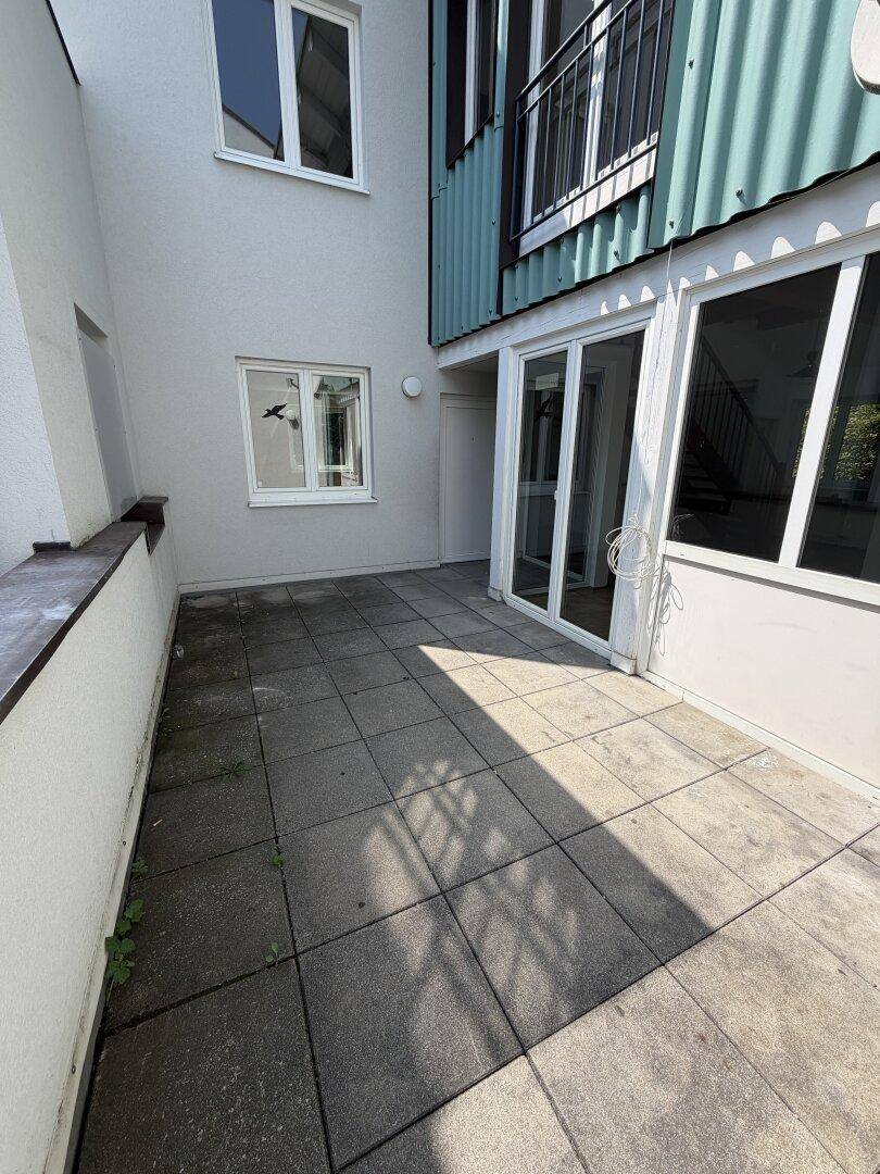Gepflasterte Terrasse im Freien neben dem Gebäude mit Zugang zu den Innenräumen.