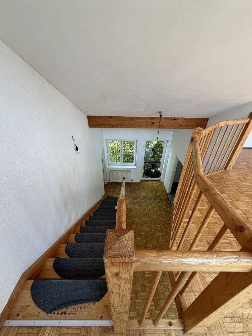 Blick von oben auf eine Holztreppe mit Teppichstufen und Parkettboden im unteren Bereich.