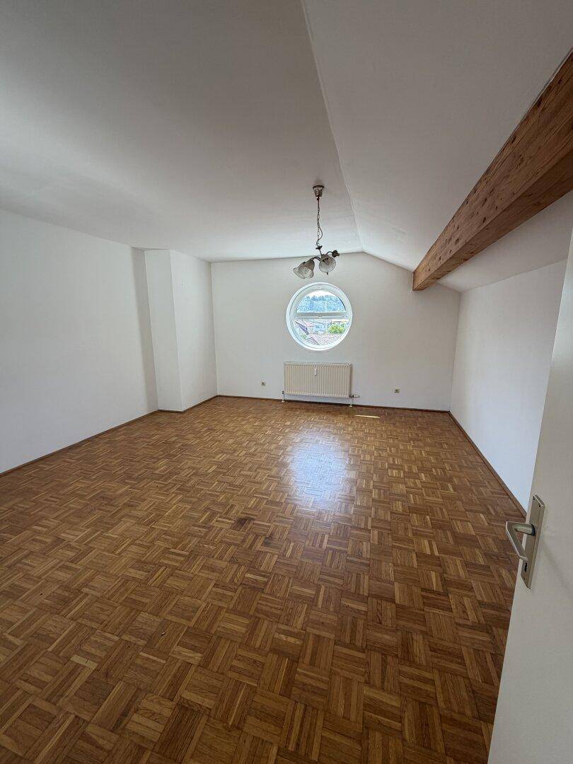 Geräumiges Zimmer mit Parkettboden, weißen Wänden und einem einzigartigen runden Fenster.