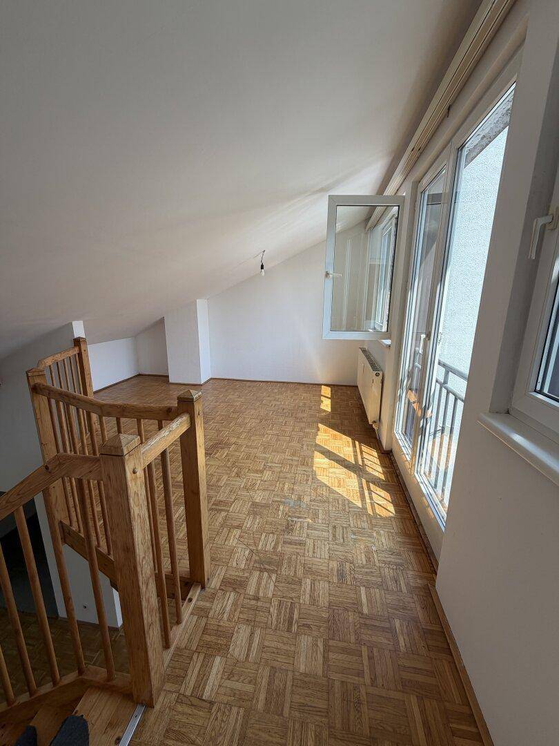 Heller Raum mit Parkettboden, Dachschräge und großen Fenstern mit französischem Balkon.