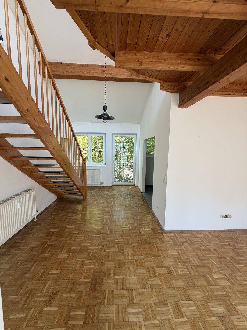 Offener Wohnbereich mit Parkettboden, sichtbaren Holzdeckenbalken und einer Holztreppe.