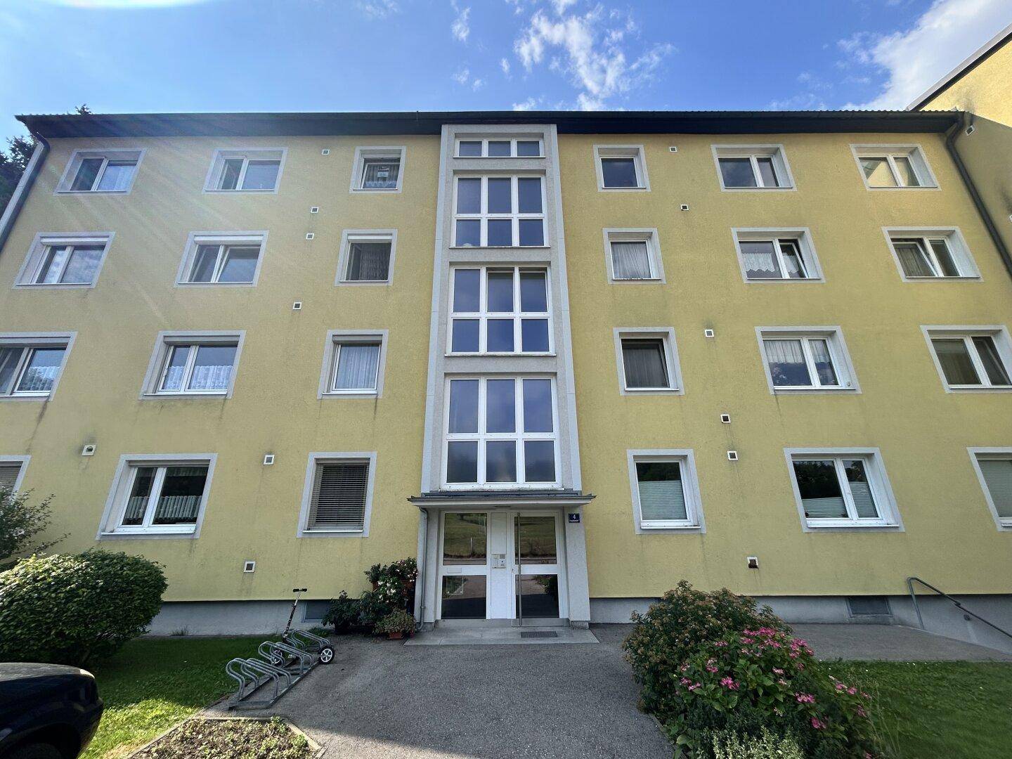 Gelbe Fassade eines Mehrfamilienhauses mit vielen Fenstern und Eingangsbereich.