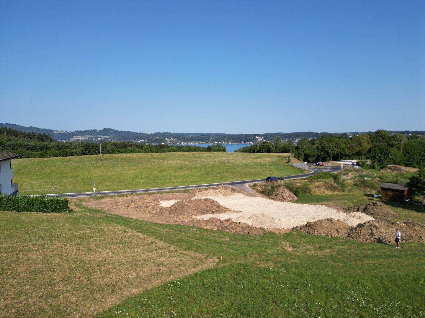 Weitläufiger Blick auf ein vorbereitetes Baugrundstück mit angrenzenden Feldern und einem Seehorizont.