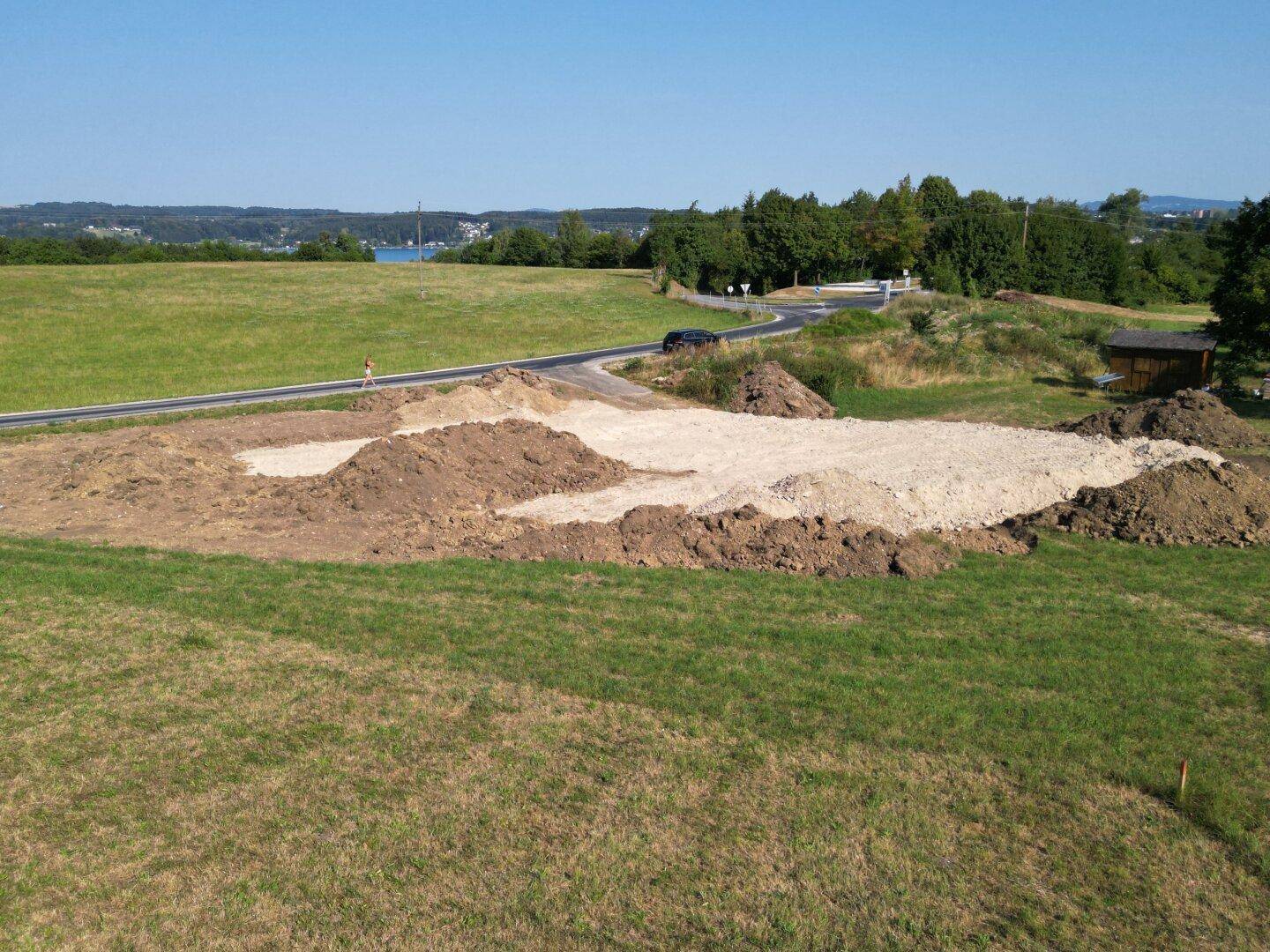 Übersicht des Baugrundstücks mit Erdarbeiten, umgeben von Natur und einem See am Horizont.
