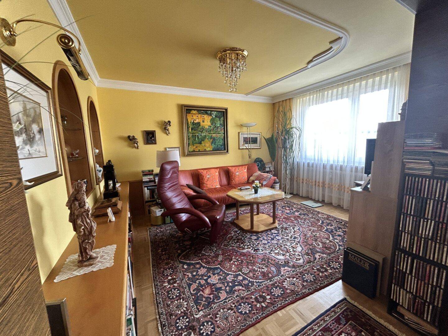 Helles Wohnzimmer mit gelben Wänden, großem Fenster und klassischem Kronleuchter.
