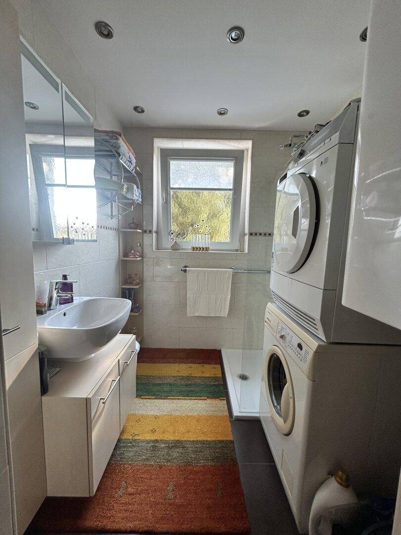 Modernes Badezimmer mit Waschbecken, Spiegelschrank, Dusche und Waschmaschine.