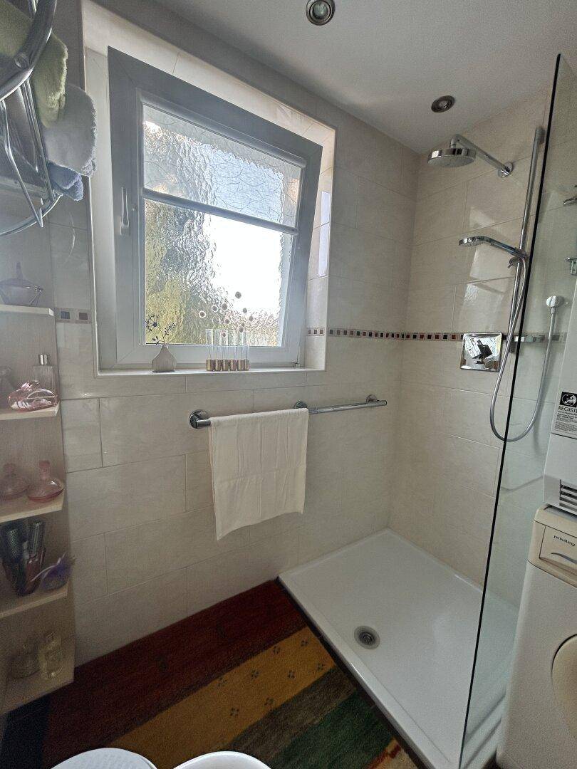 Duschbereich im Badezimmer mit Regendusche, Glasabtrennung und Haltegriff.