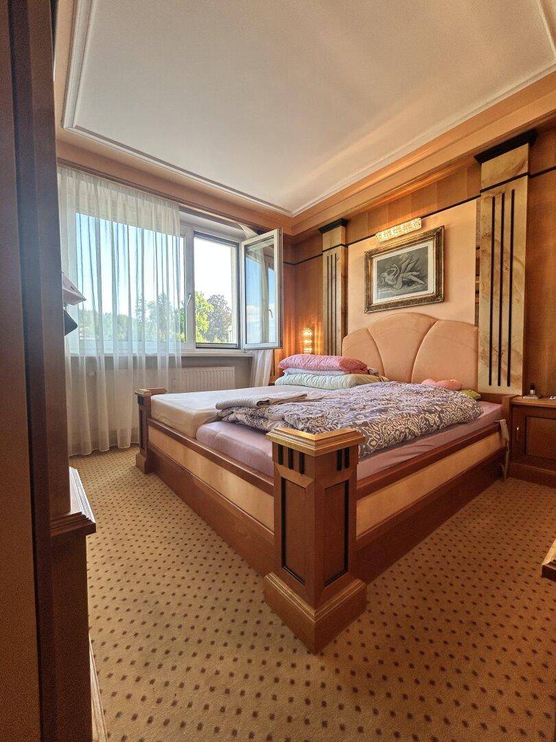 Geräumiges Schlafzimmer mit Doppelbett, Teppichboden und Fenster mit Blick ins Grüne.