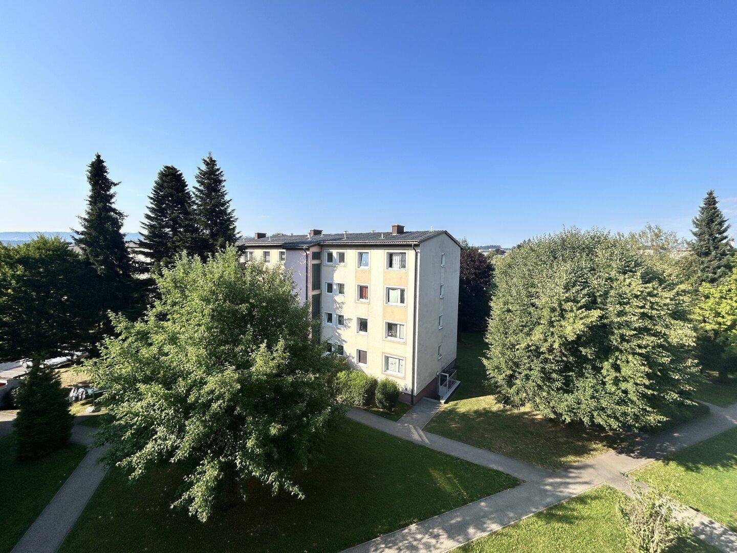 Mehrfamilienhaus in grüner Umgebung mit Bäumen und gepflegten Rasenflächen.
