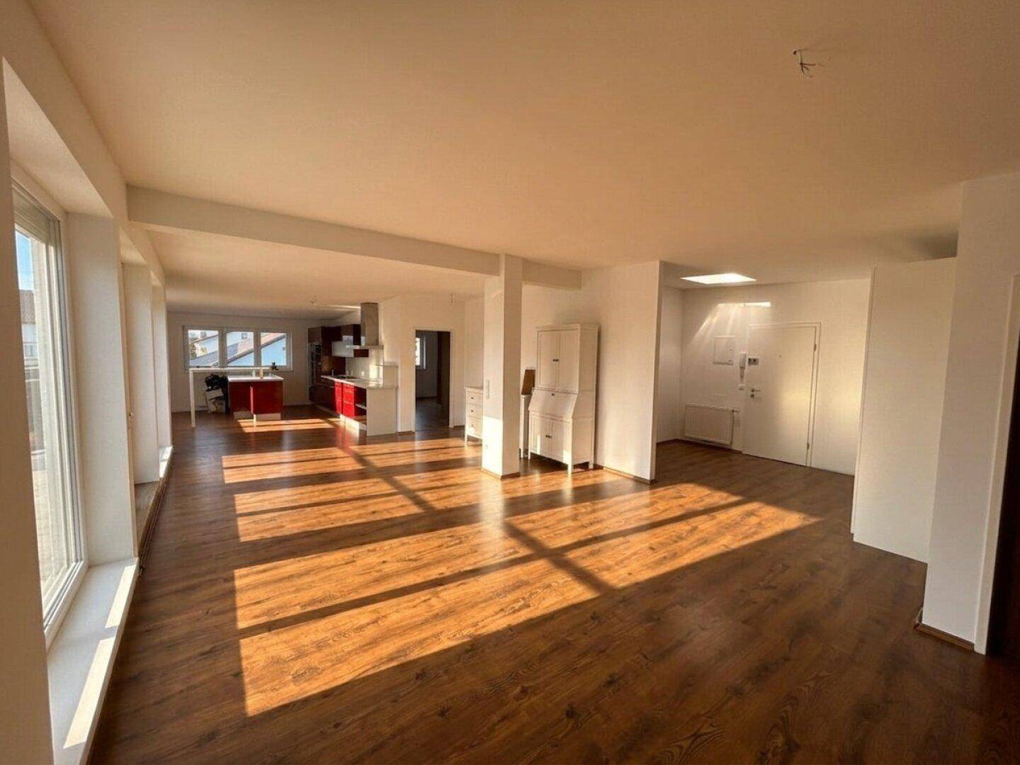 Lichtdurchfluteter, offener Wohnbereich mit Holzboden und moderner Küche im Hintergrund.