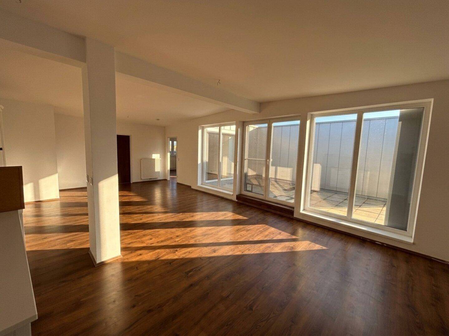 Geräumiger, offener Wohnbereich mit Holzboden, viel Tageslicht und Zugang zur Außenterrasse.