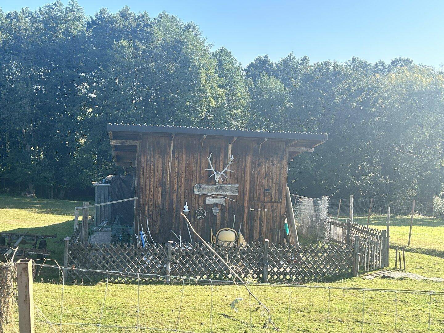 Vorderansicht des Holzschuppens mit rustikaler Dekoration und einem Lattenzaun im sonnigen Grünen.