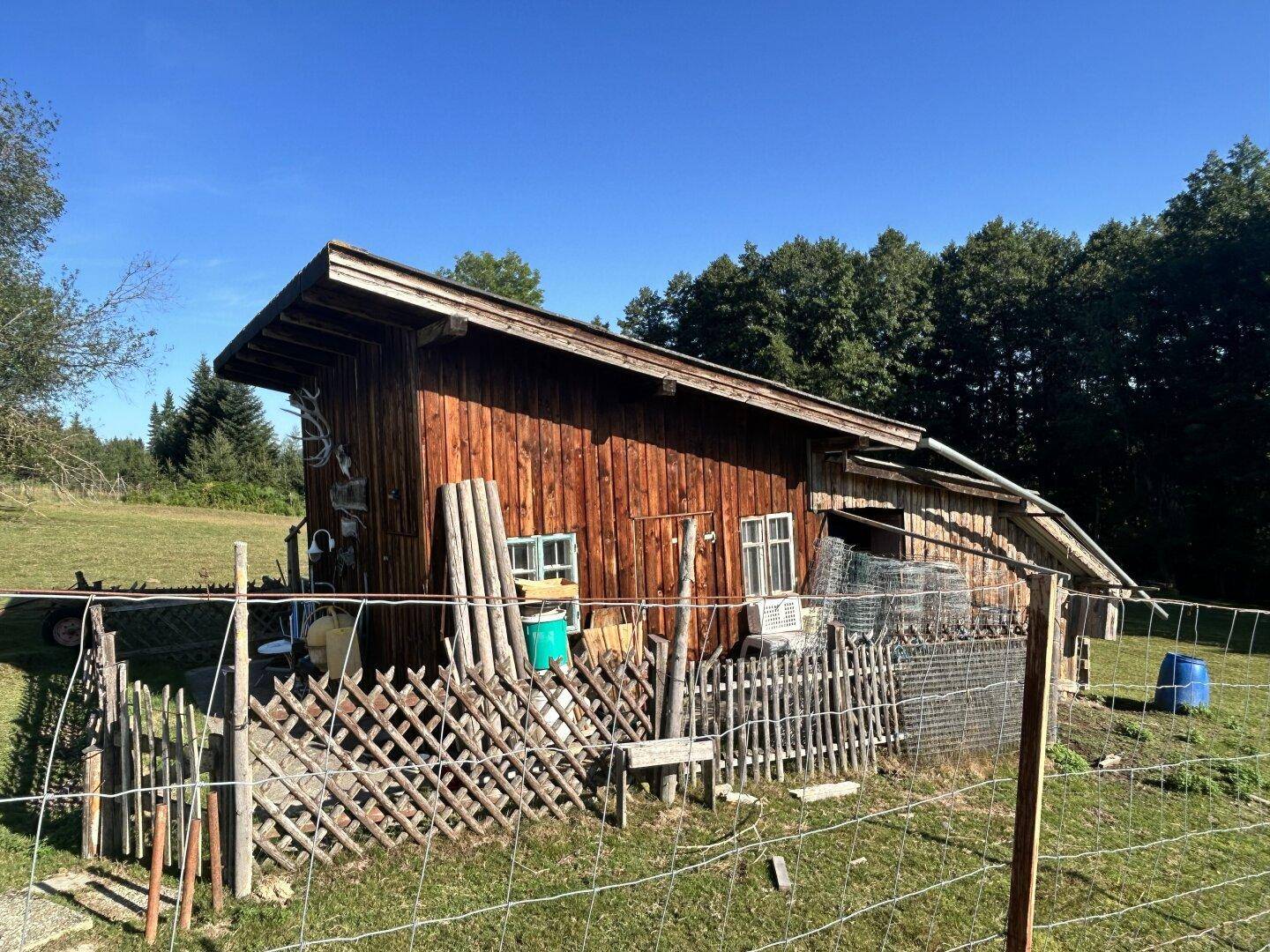 Seitenansicht des rustikalen Holzschuppens mit kleinen Fenstern und einem Lattenzaun im Vordergrund.