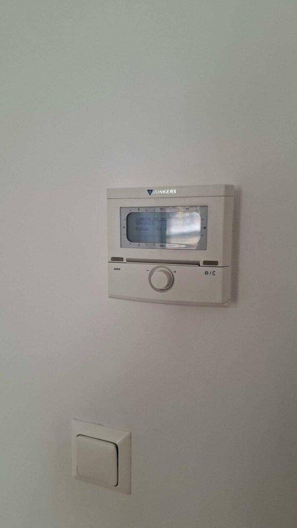 Nahaufnahme eines Junkers-Thermostats an einer weißen Wand.