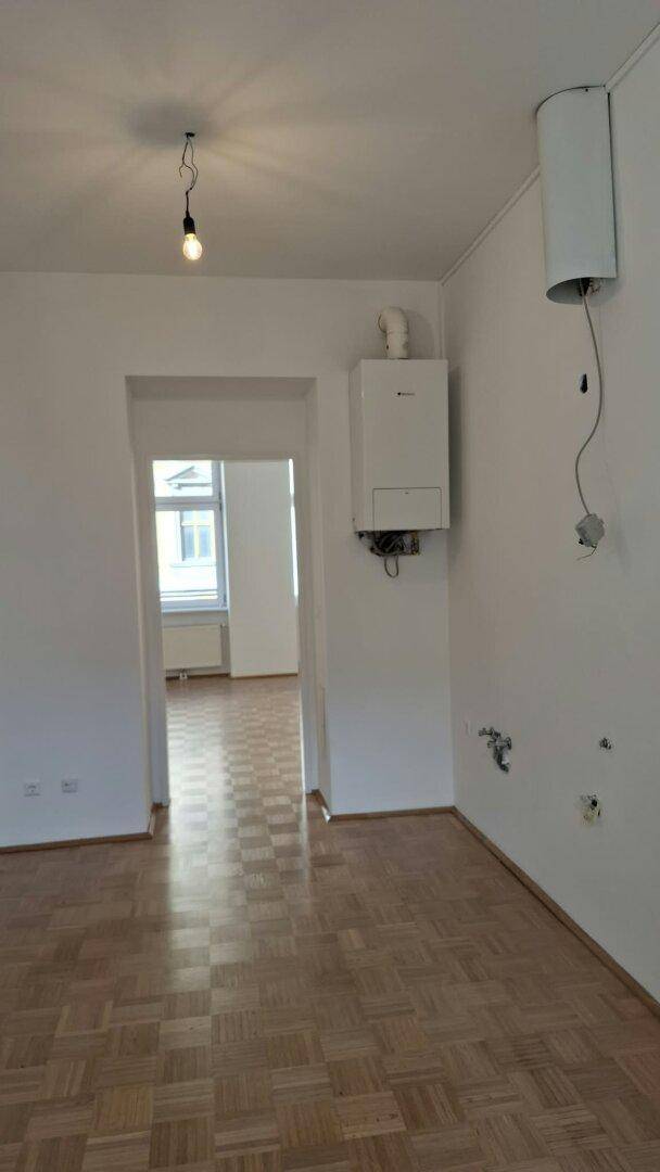 Raum mit Parkettboden, Heiztherme und Anschlüssen für eine zukünftige Küche.