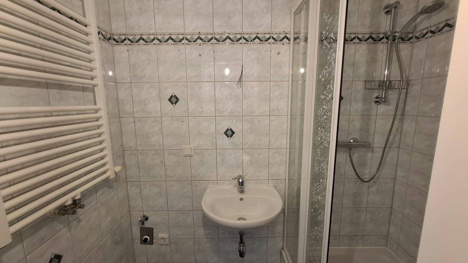 Badezimmer mit Duschkabine, Waschbecken und beheiztem Handtuchhalter, gefliest in hellen Tönen.