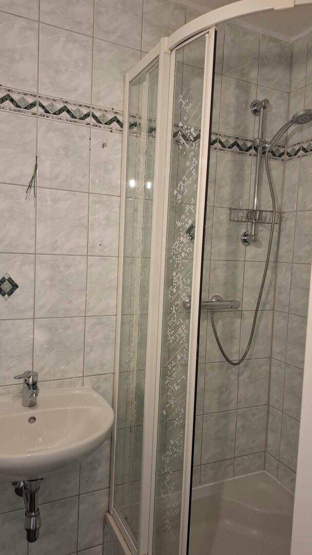 Badezimmer mit Duschkabine und Waschbecken, gefliest in hellen Tönen mit dekorativer Bordüre.
