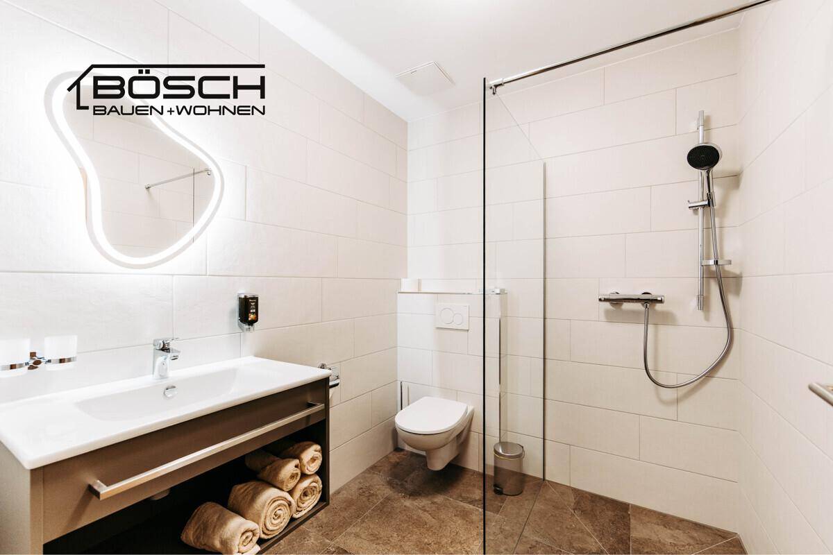 Modernes Badezimmer mit begehbarer Dusche, Wand-WC und beleuchtetem Spiegel.