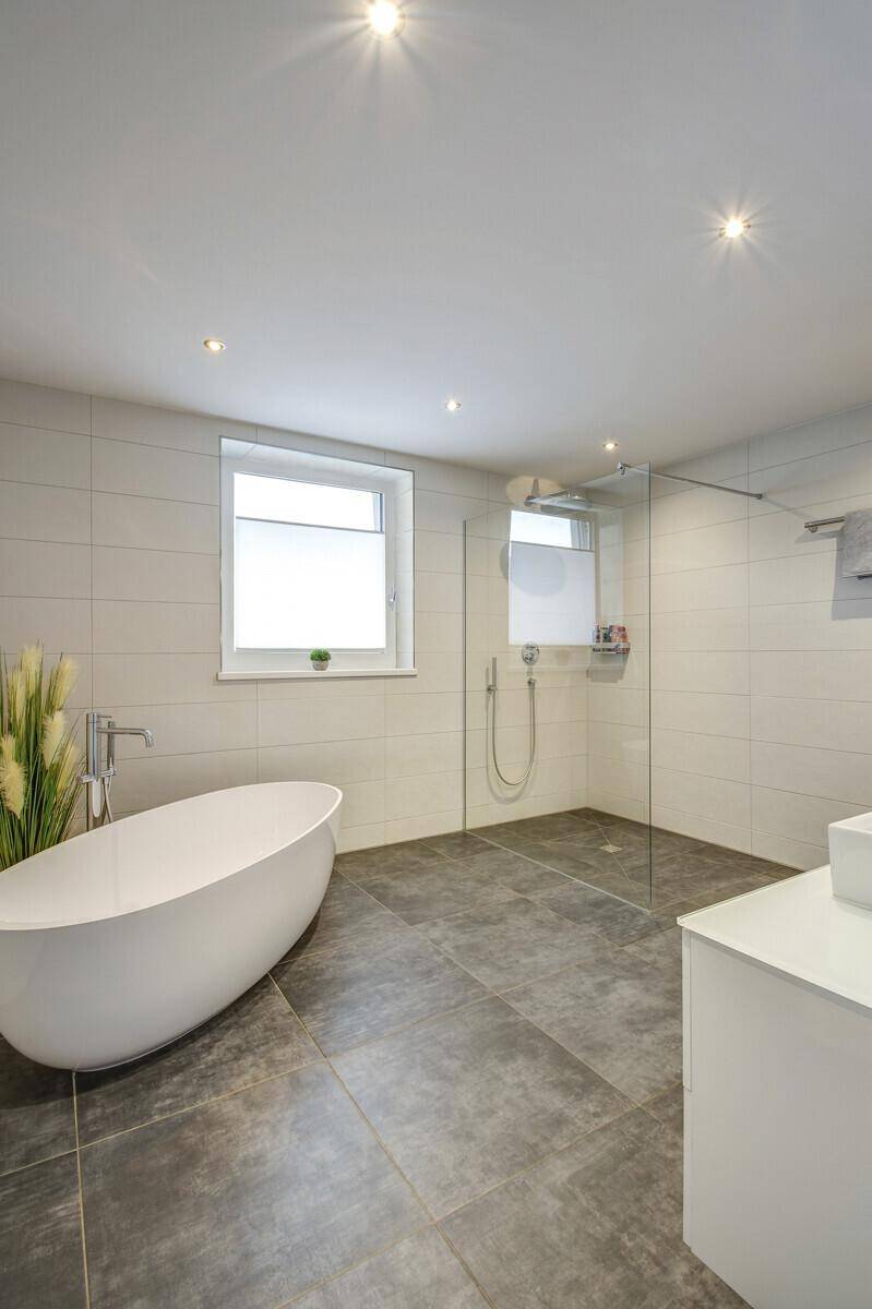 Modernes Badezimmer mit freistehender Badewanne, großer begehbarer Dusche und Fenster.