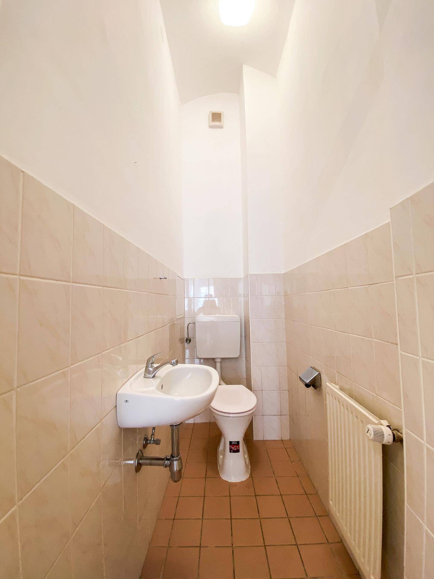 Kleines Gäste-WC mit beigefarbenen Fliesen, einem Wand-WC und einem kompakten Handwaschbecken.
