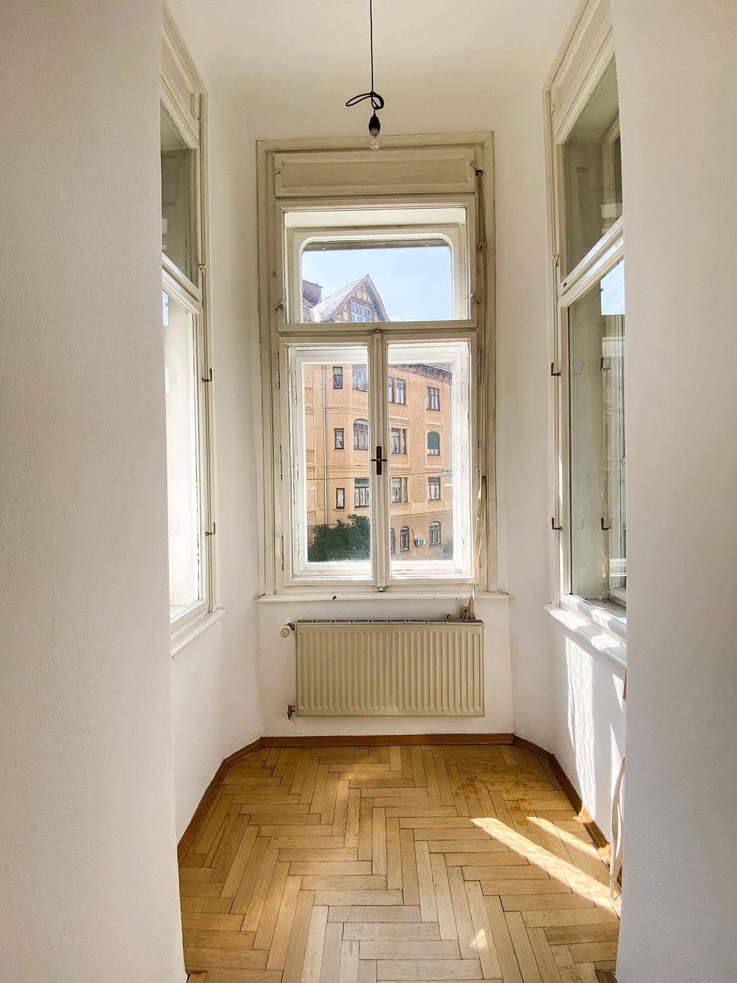 Gemütlicher Erkerbereich mit Fischgrätparkett und einem großen Fenster, das einen Blick nach draußen bietet.