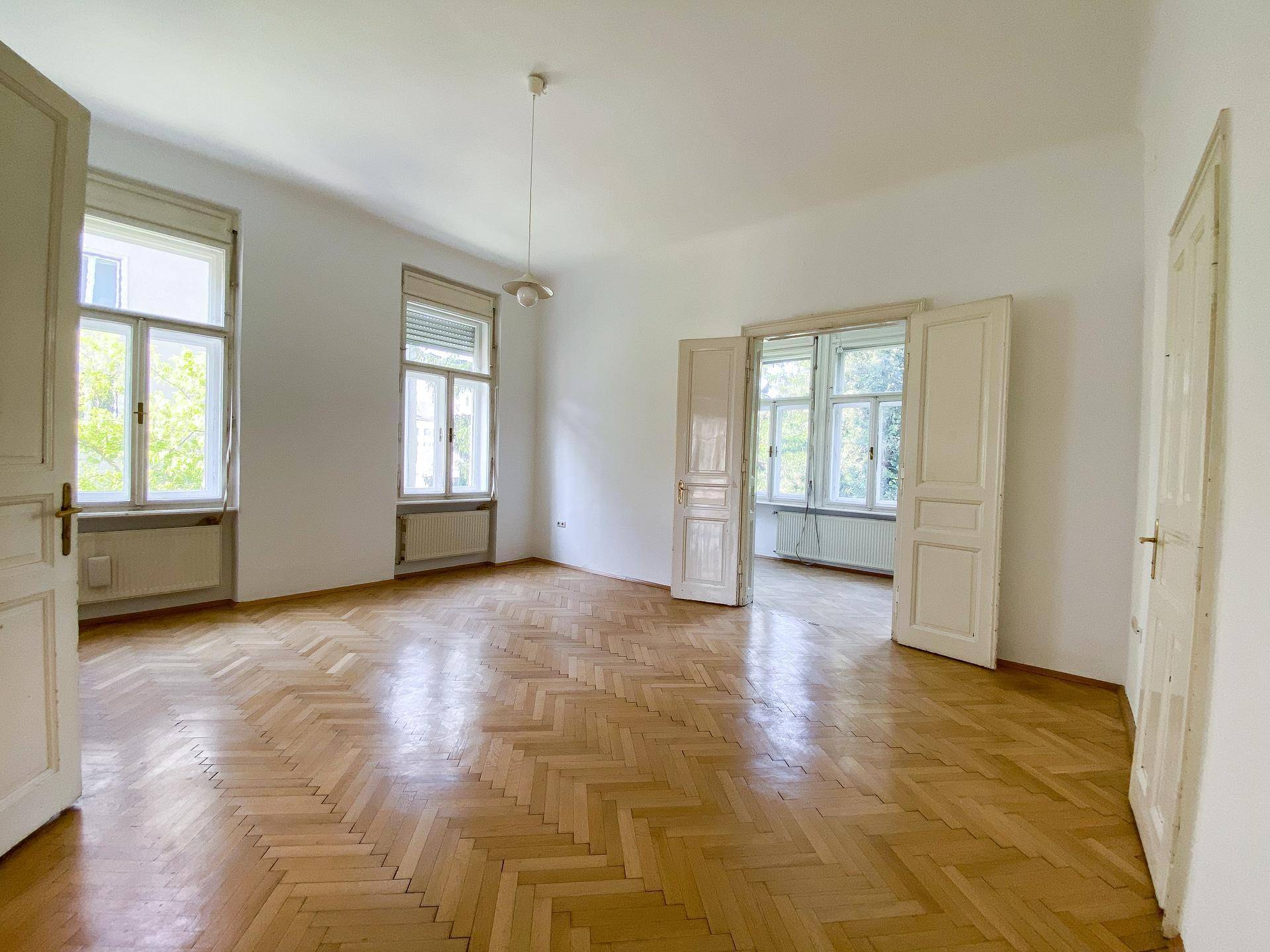 Geräumiges Schlafzimmer mit Fischgrätparkett und hohen Fenstern, die den Raum hell und luftig wirken lassen.