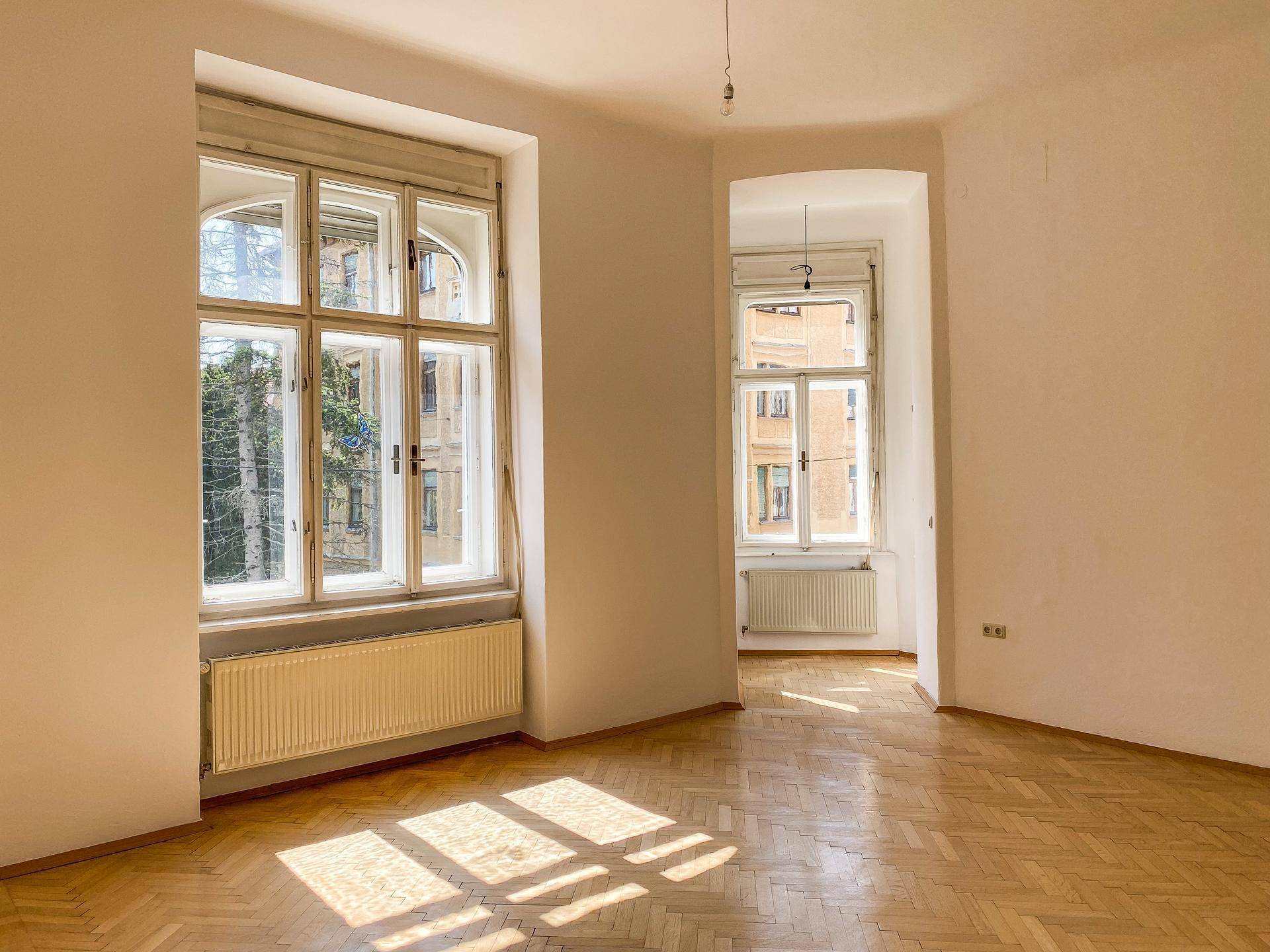 Heller Raum mit Fischgrätparkett und einem Erkerbereich, der durch große Fenster viel Licht erhält.