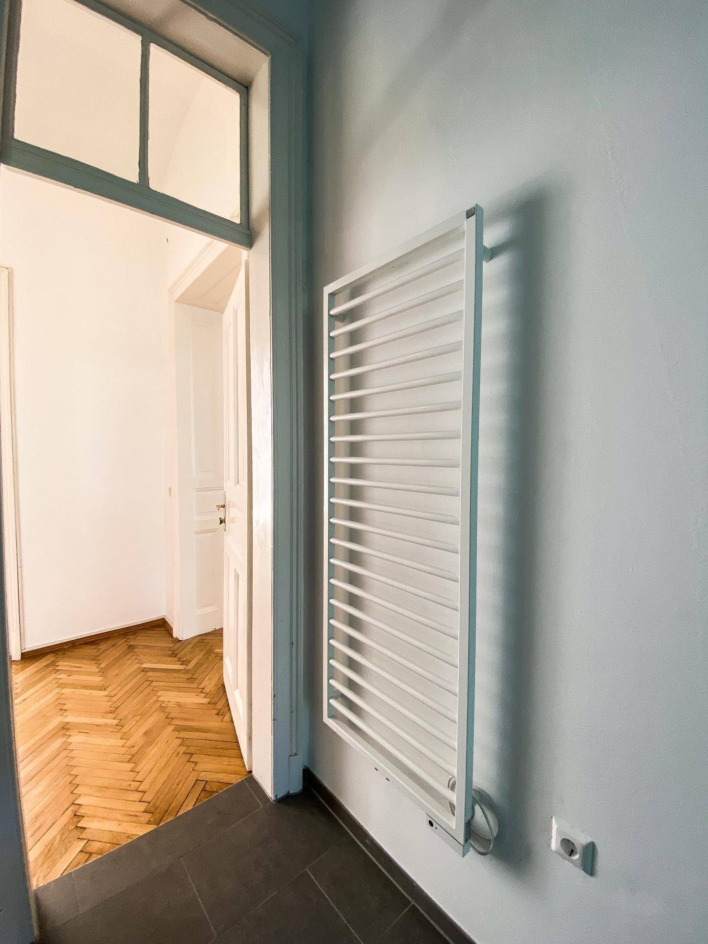Detailansicht eines modernen Handtuchheizkörpers an einer hellblauen Wand im Badezimmer.