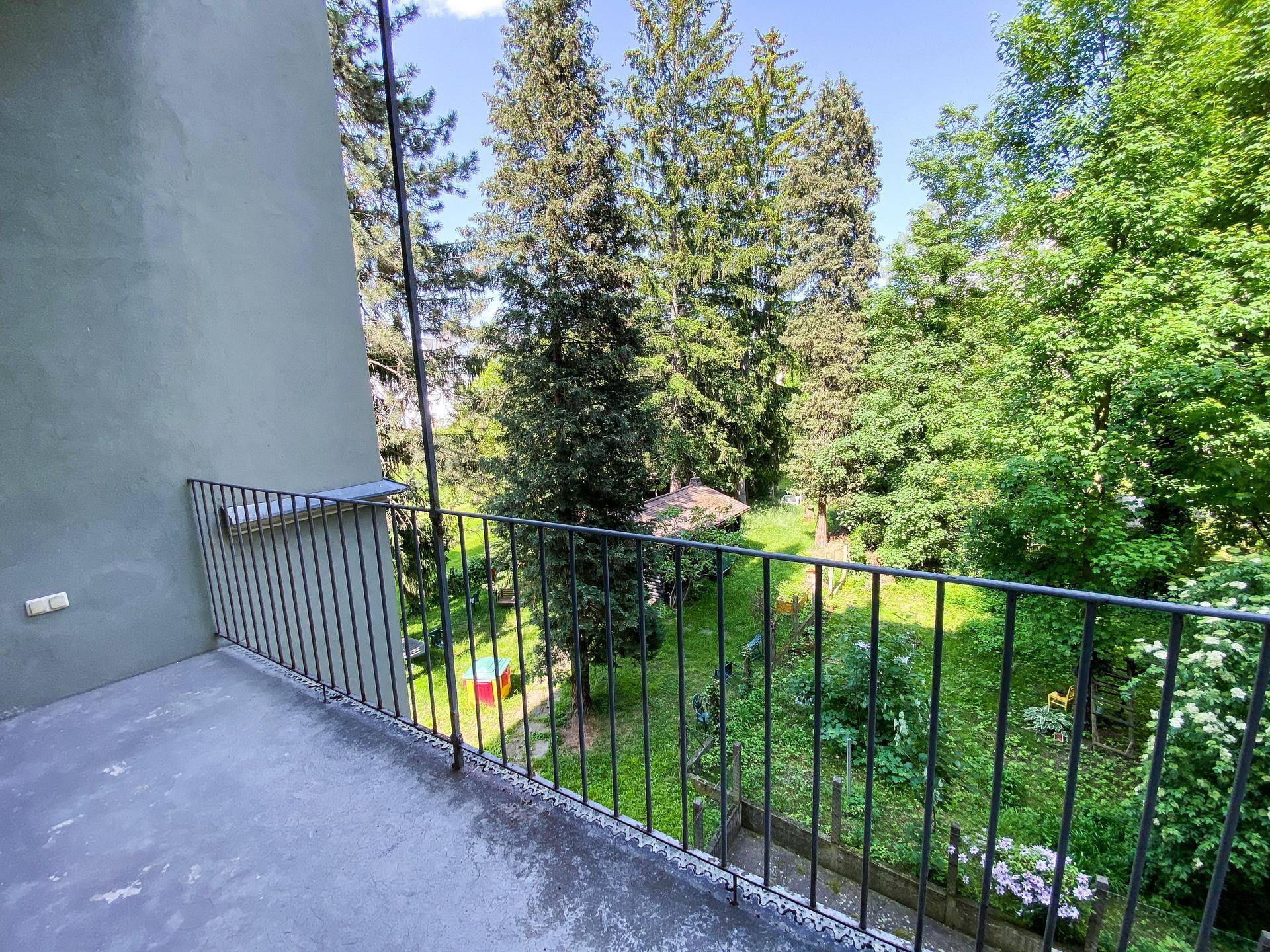 Balkon mit schmiedeeisernem Geländer und weitem Blick auf einen üppigen, grünen Gartenbereich.