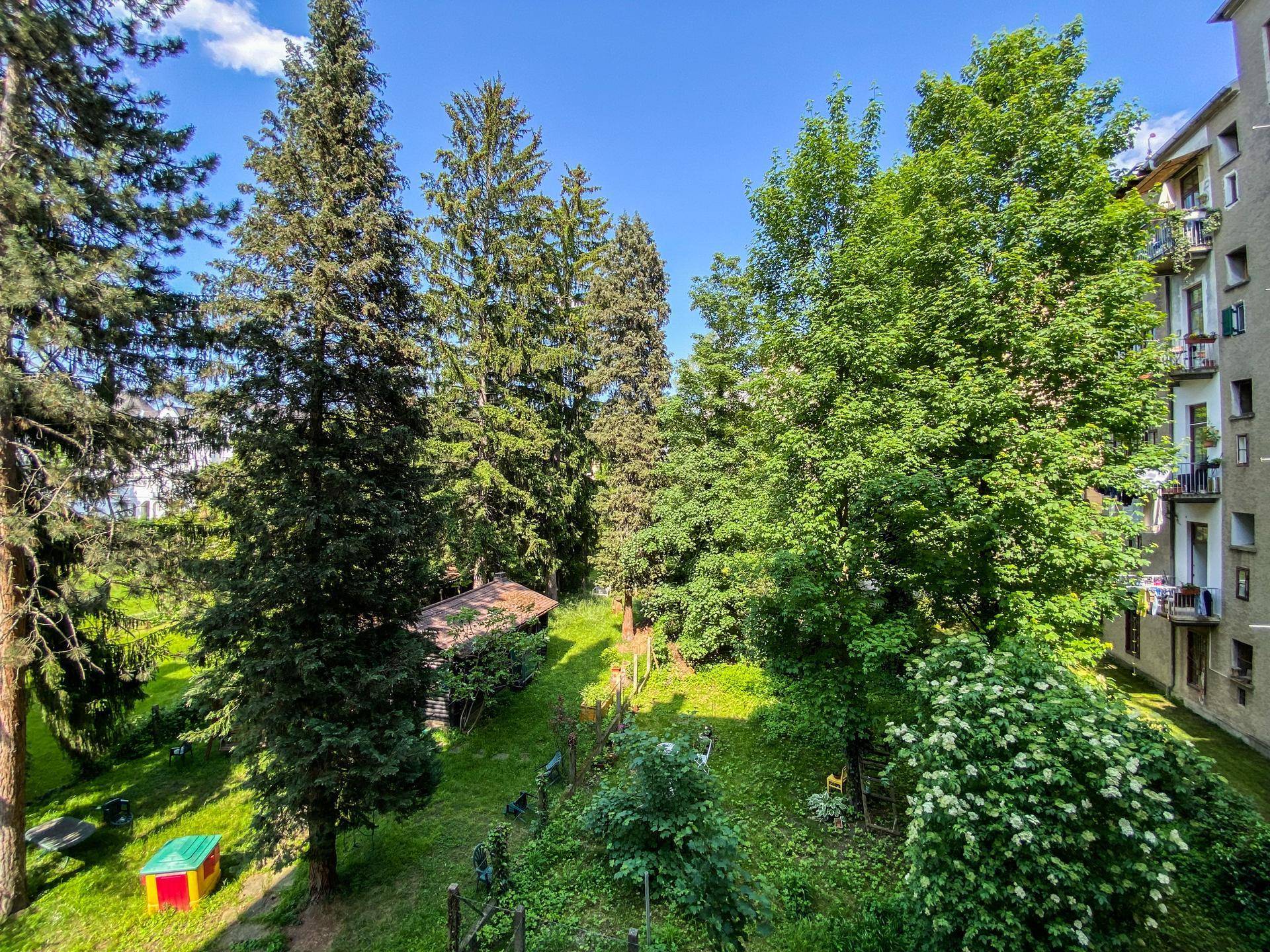 Panoramablick von einem Balkon auf einen weitläufigen, grünen Garten mit hohen Bäumen und viel Natur.