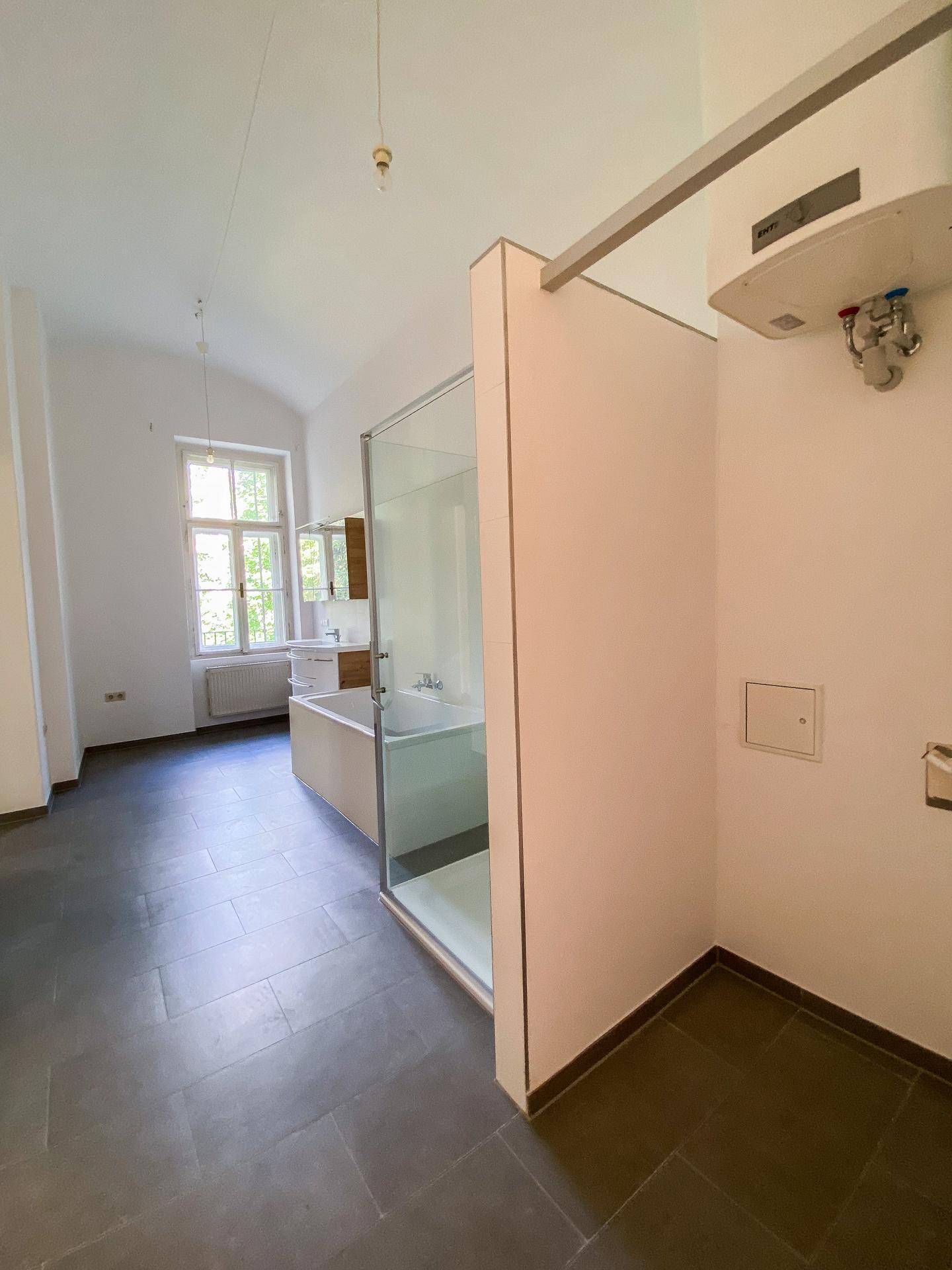 Badezimmer mit Duschkabine, Badewanne und einem Warmwasserbereiter an der Wand.
