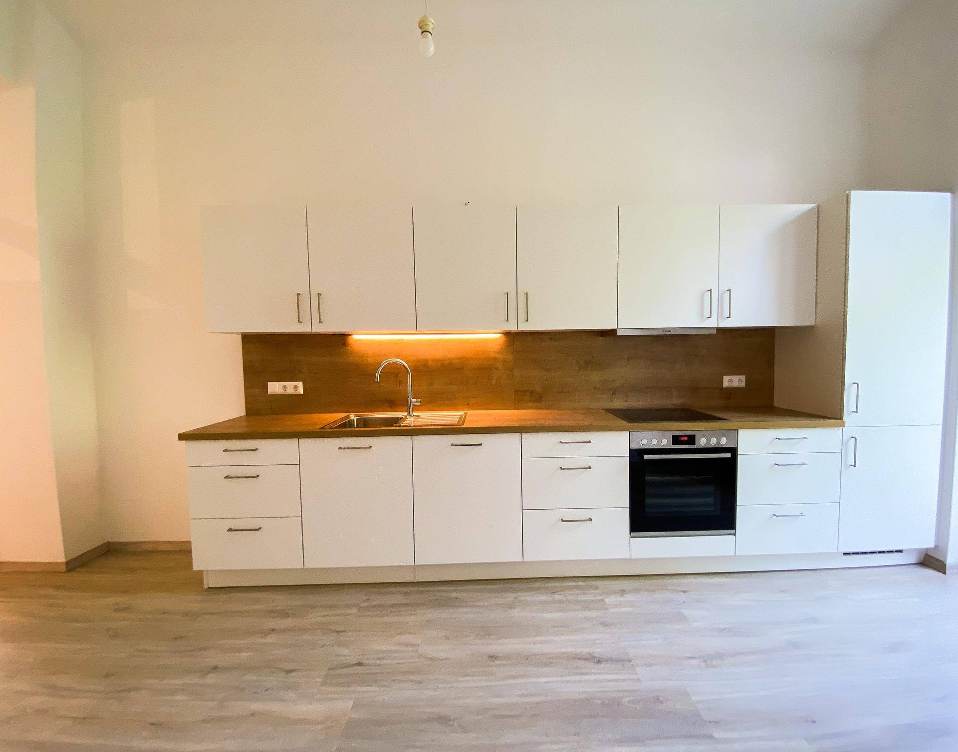 Moderne Einbauküche mit weißen Schränken, Holzoptik-Arbeitsplatte und integrierten Geräten.