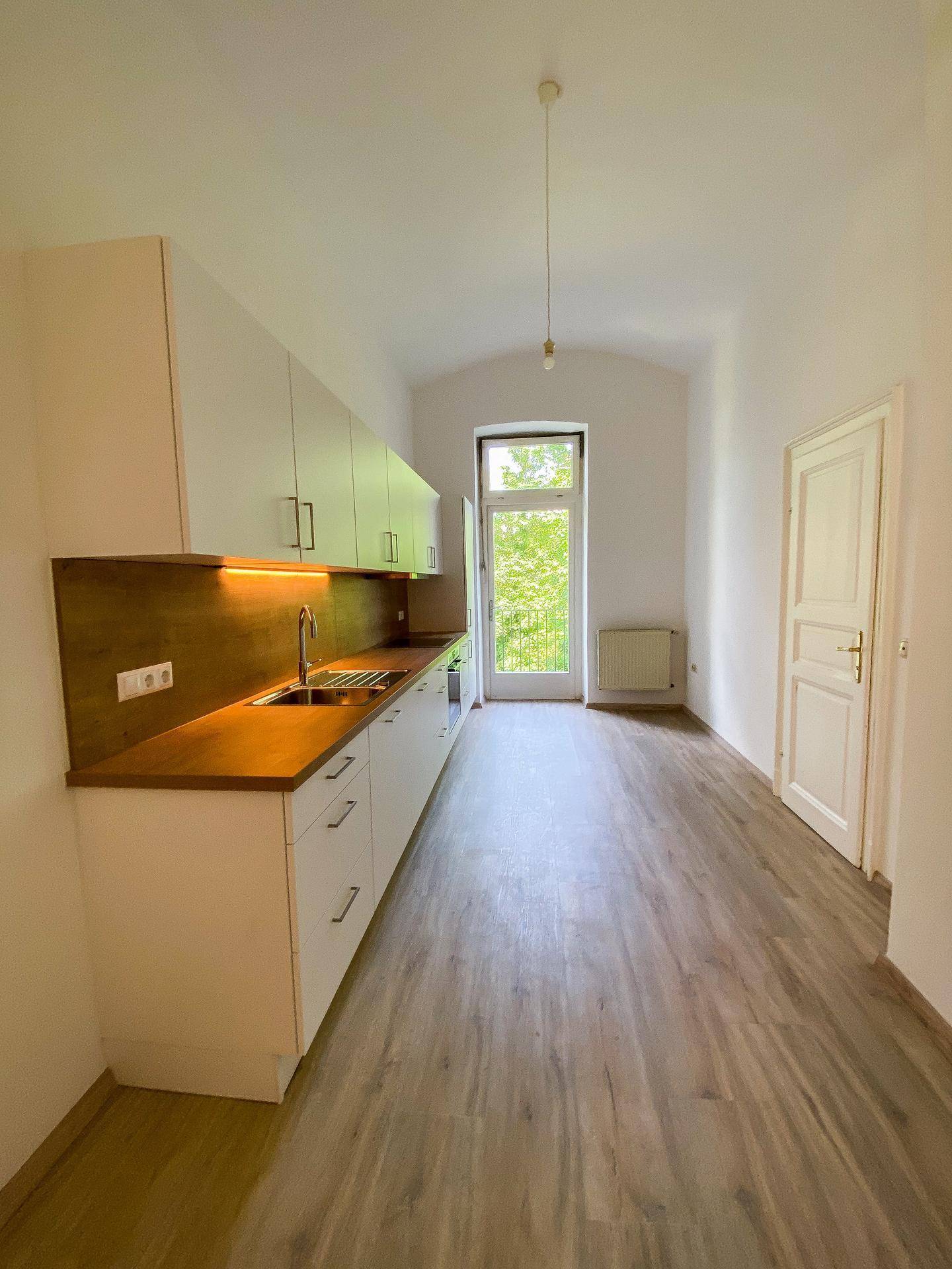 Längliche Küche mit Einbaumöbeln, Laminatboden und Zugang zu einem Balkon durch eine Fenstertür.