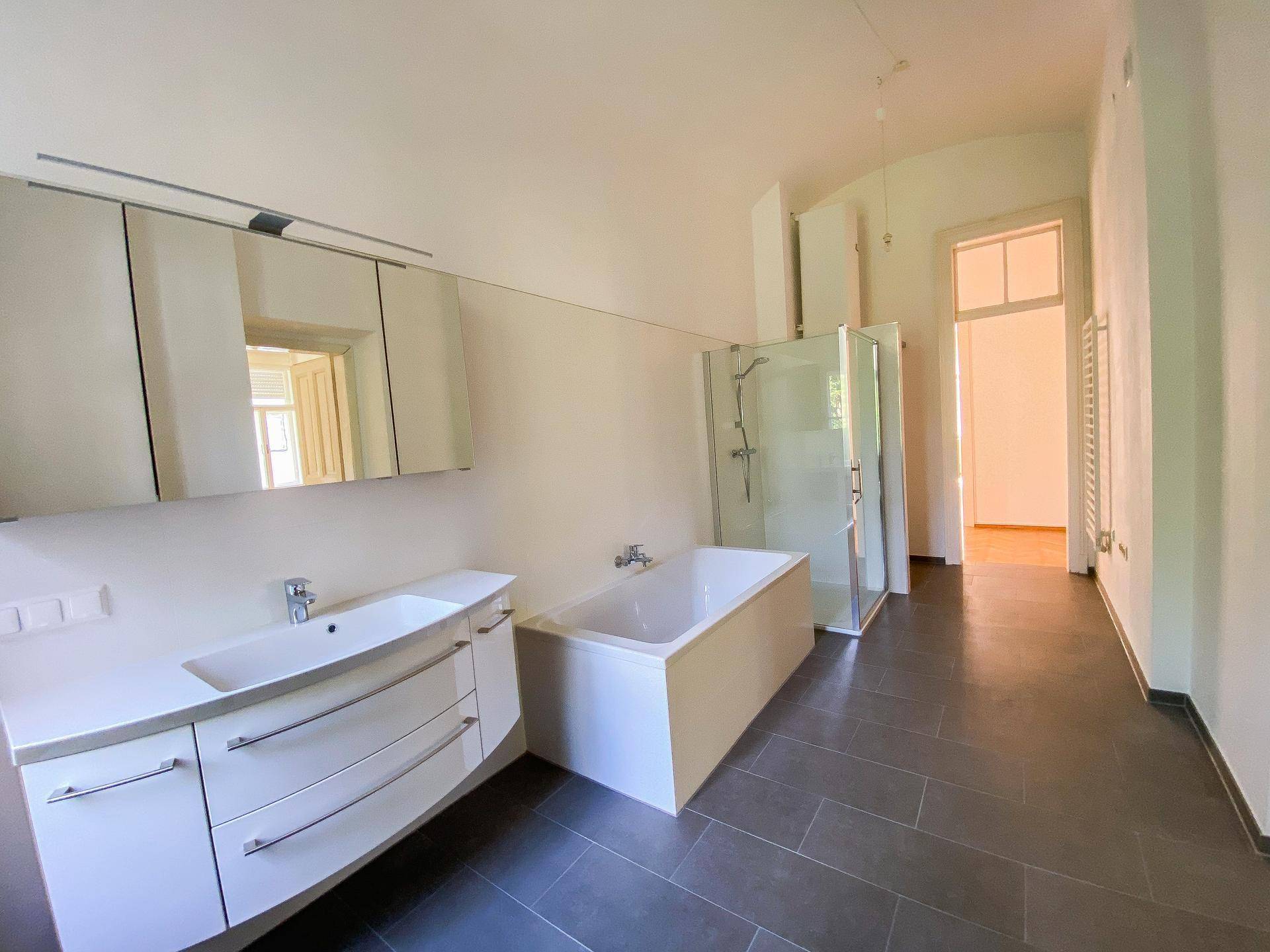 Helles Badezimmer mit Doppelwaschtisch, Spiegelschrank, Badewanne und einer modernen Duschkabine.