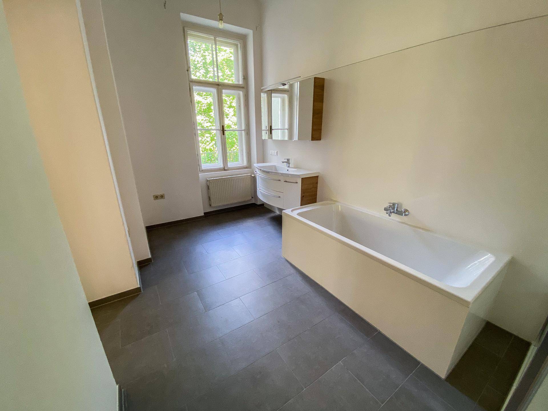Geräumiges Badezimmer mit Badewanne, Waschtisch und einem großen Fenster, das für natürliche Belüftung sorgt.