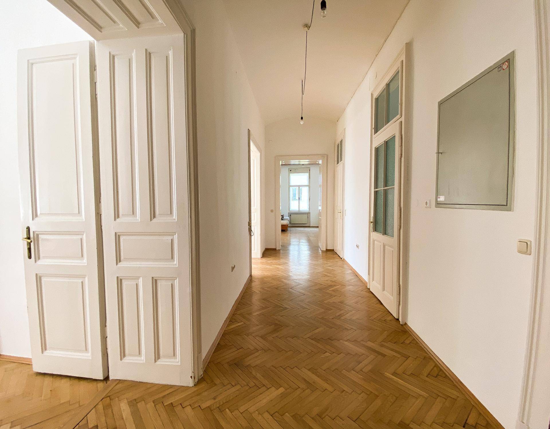 Langer Flur mit Fischgrätparkett und hohen Türen, der zu verschiedenen Räumen der Wohnung führt.