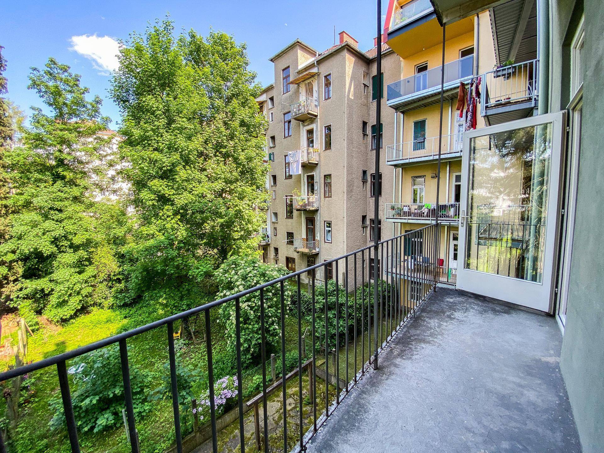 Geräumiger Balkon mit Blick auf einen grünen Garten und hohe Bäume, ideal zum Entspannen im Freien.