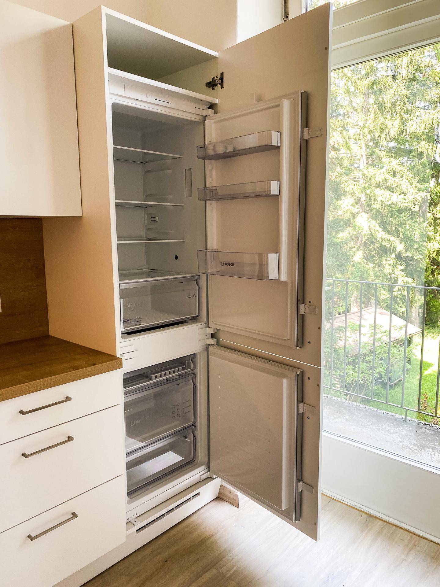 Integrierter Kühlschrank in der Küche mit geöffneter Tür, zeigt den Innenraum und den Blick nach draußen.