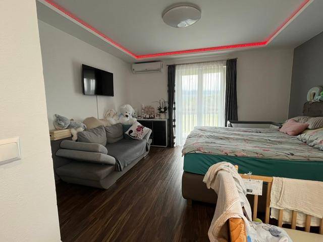 Schlafzimmer mit Doppelbett, Sofa, Holzboden und indirekter Deckenbeleuchtung, hell und modern.