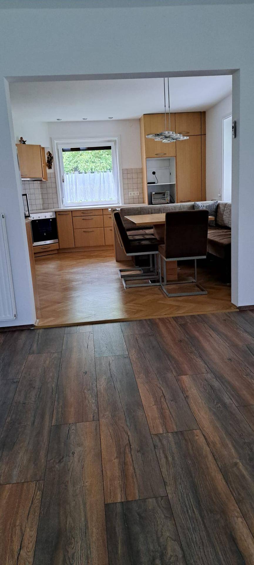 Übergangsbereich von einem Zimmer zur hellen Küche mit Essbereich und Fenster.