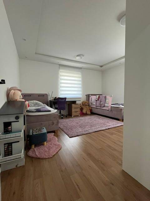 Kinderzimmer mit Holzboden, zwei Betten und einem Schreibtisch, hell und freundlich gestaltet.