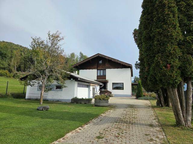 Wohnhaus mit separater Garage und langer gepflasterter Zufahrt, umgeben von Bäumen und Rasen.
