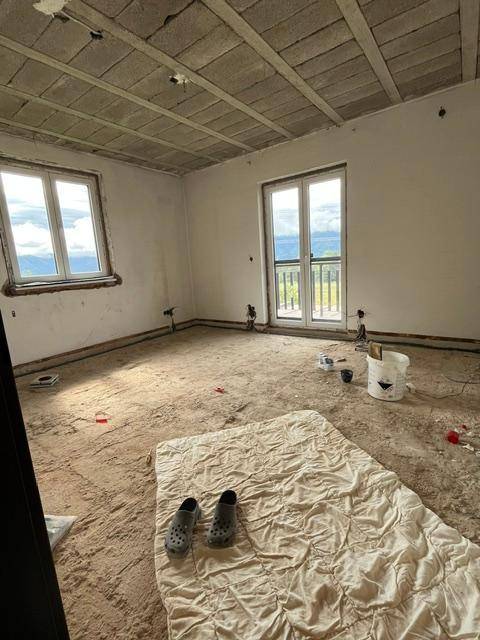Raum im Rohbauzustand mit Fenstern und Balkontür, bereit für den Innenausbau.