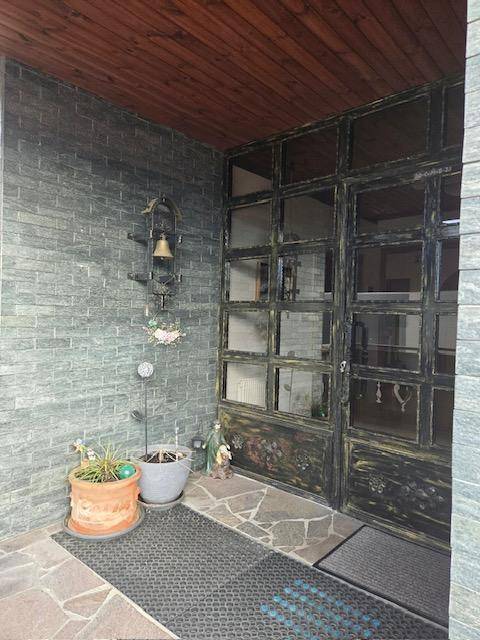 Eingangsbereich mit rustikaler Metalltür und Steinwandverkleidung, geschützt durch ein Holzdach.