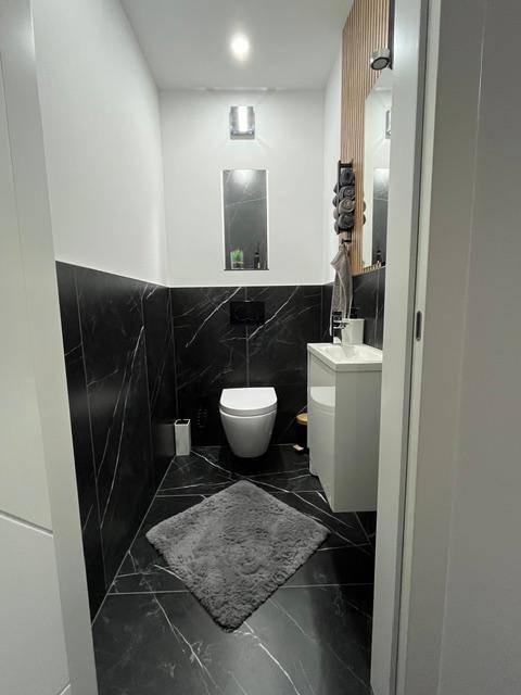 Modernes Gäste-WC mit schwarzen Marmorfliesen, Wand-WC und Einzelwaschbecken.