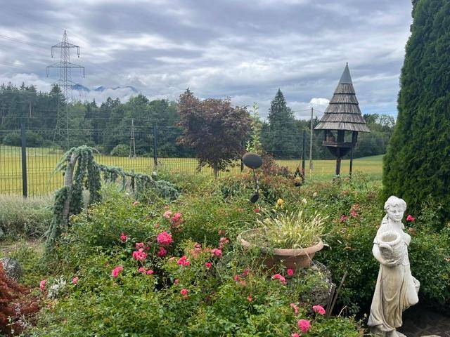 Gepflegter Garten mit Vogelhaus, blühenden Pflanzen und Blick auf die umliegende Natur und Berge.