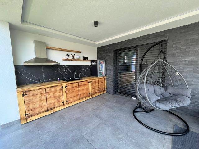 Überdachte Terrasse mit Außenküche, Holzschränken und gemütlichem Hängesessel.