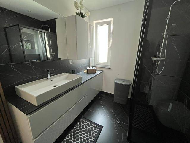 Modernes Badezimmer mit schwarzem Marmorboden, großem Waschtisch und Fenster für Tageslicht.