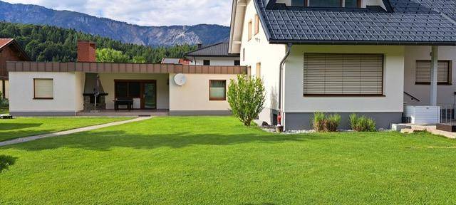 Weitläufiger Rasenbereich vor der Hausfassade mit angrenzender Terrasse und Bergblick.