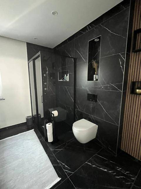 Modernes Badezimmer mit schwarzen Marmorfliesen, begehbarer Dusche und Wand-WC.